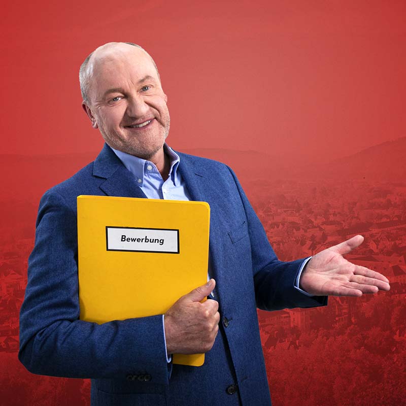 Bodo Bach präsentiert eine gelbe Bewerbungsmappe – humorvolle Werbekampagne für Jobbewerbungen