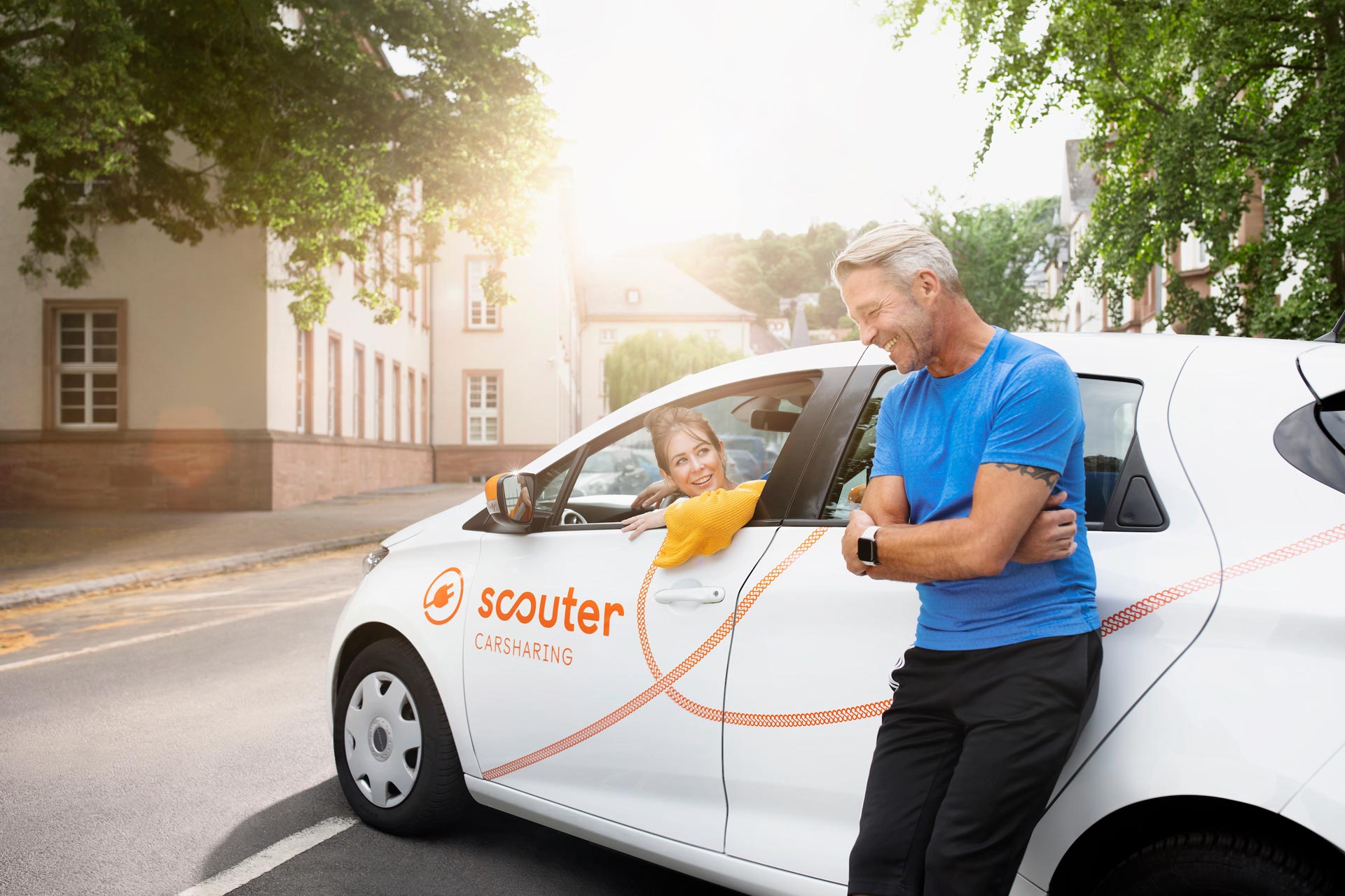 Ein Mann der an einem Auto lehnt und eine junge Frau am Steuer. Im Hintergrund der Sonnenuntergang